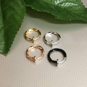 May include: Four non-piercing hoop earrings in gold, silver, rose gold, and black. Each earring has a twisted design and a small post closure. The earrings are displayed on a light gray surface with a green leaf in the background.