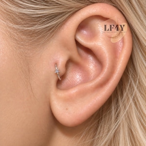 May include: A silver-toned hoop earring featuring a small, star-shaped charm with a central clear stone. The earring is inserted into the tragus piercing of an ear. The text LF4Y HAND CRAFTED BODY JEWELLERY is visible in the upper right corner.