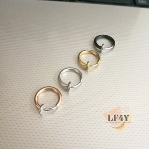 Puede incluir: Cuatro anillos de nariz sin perforación en oro rosa, plata, oro y negro. Cada anillo tiene un diseño circular simple con un pequeño poste recto. Los anillos se muestran sobre una superficie clara y texturizada.
