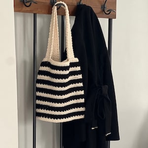 Puede incluir: Una bolsa de mano de crochet a rayas blancas y negras colgada de un perchero.