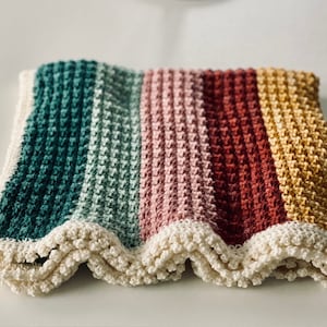 May include: A handmade crochet blanket with a striped pattern in teal, light green, pink, red, and yellow. The blanket has a scalloped, off-white border. The textured stitch creates a cozy, soft appearance.