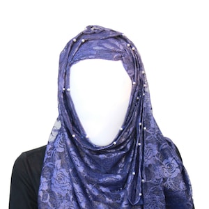 May include: A dark blue lace hijab with pearl embellishments. The hijab is draped over a mannequin's head and shoulders.