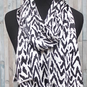 May include: A black and white patterned scarf draped over a black mannequin. The scarf features a bold zebra-like print. The fabric is lightweight and appears to be flowing. The scarf is a fashion accessory.