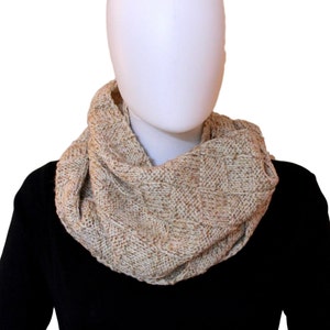 May include: A beige knitted infinity scarf with a textured pattern. The scarf is worn by a mannequin with a black shirt.