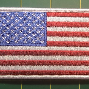 May include: White embroidered patch of the American flag with red and blue stars and stripes.
