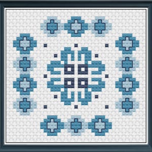 May include: A framed cross-stitch design featuring a geometric pattern in shades of blue on a white background. The design includes a central circular motif surrounded by repeating cross shapes and square accents. The frame is a dark blue.