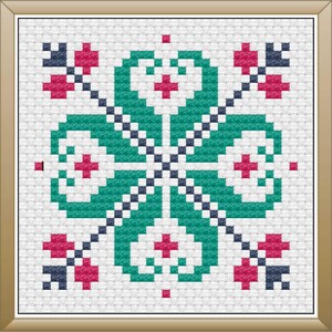 May include: Framed cross-stitch artwork featuring a symmetrical floral design. The central motif is a four-leaf clover shape in teal, with red and navy accents. The background is a white fabric, and the frame is a light brown color.