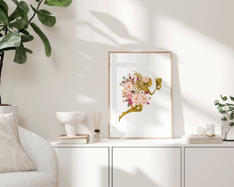 May include: A gold silhouette of a fairy with pink and purple flowers, holding a tooth, in a framed print.