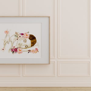 May include: A watercolour painting of a woman with a floral crown sleeping on a bed of flowers. The painting is framed in a light wood frame and is hanging on a white wall.