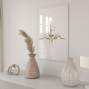 May include: A white framed print with a gold EKG line and floral accents. The EKG line is labeled with the letters P, Q, R, S, and T. The print is displayed on a white shelf with a vase of dried pampas grass and a decorative object.