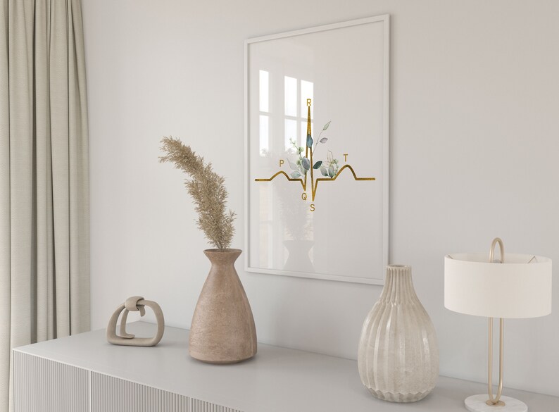 May include: A white framed print with a gold EKG line and floral accents. The EKG line is labeled with the letters P, Q, R, S, and T. The print is displayed on a white shelf with a vase of dried pampas grass and a decorative object.