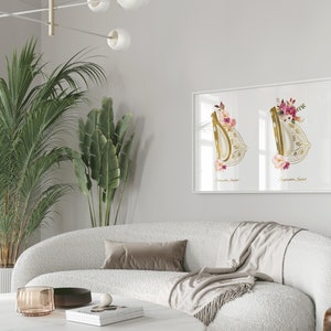 May include: A white framed print with two watercolor illustrations of a golden, ornate, floral design. The design is reminiscent of a traditional bridal veil. The print is hanging on a white wall above a white couch.