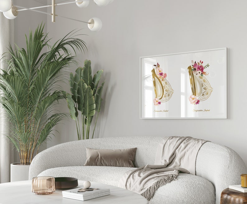 May include: A white framed print with two watercolor illustrations of a golden, ornate, floral design. The design is reminiscent of a traditional bridal veil. The print is hanging on a white wall above a white couch.
