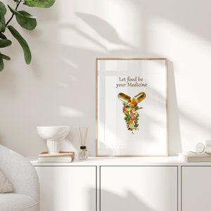 May include: A framed print with a white background and the text "Let food be your medicine". The image shows two gold capsules filled with colorful fruits and vegetables.