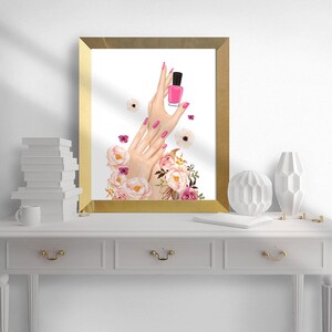 May include: A gold framed print with a watercolor illustration of hands holding a pink nail polish bottle. The hands are surrounded by pink and white flowers.