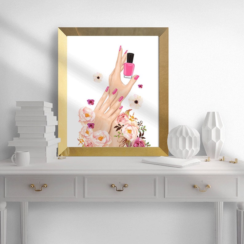 May include: A gold framed print with a watercolor illustration of hands holding a pink nail polish bottle. The hands are surrounded by pink and white flowers.