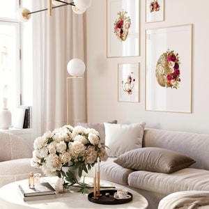 May include: A living room interior with a white couch, a white coffee table, and a bouquet of white peonies in a vase. Four framed prints of anatomical hearts with floral accents hang on the wall.