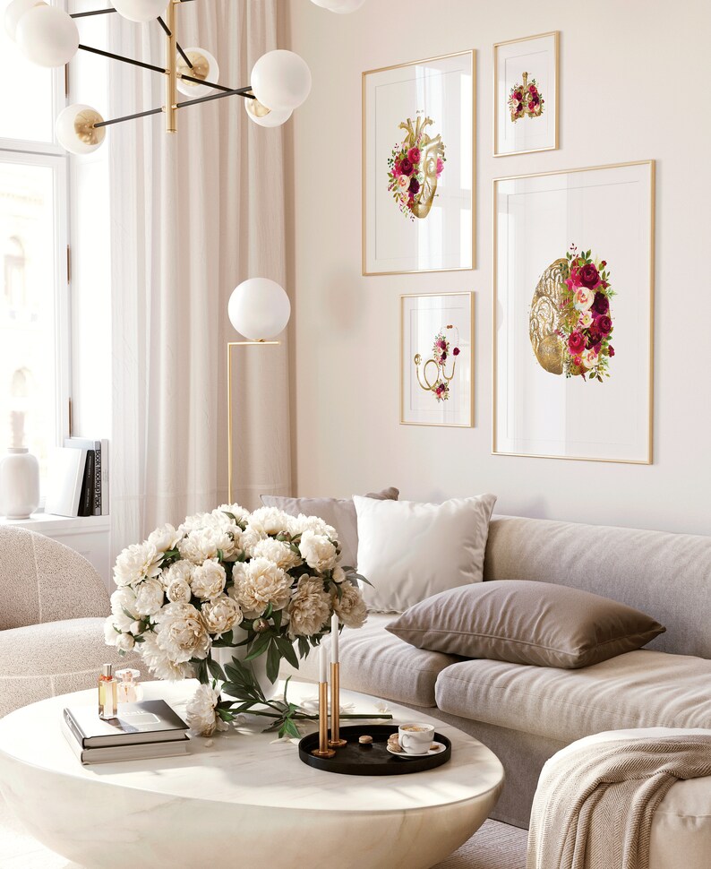 May include: A living room interior with a white couch, a white coffee table, and a bouquet of white peonies in a vase. Four framed prints of anatomical hearts with floral accents hang on the wall.