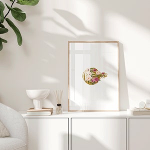 May include: A framed print of a floral design with pink, white, and gold flowers on a gold background. The print is in a light wood frame and is hanging on a white wall.