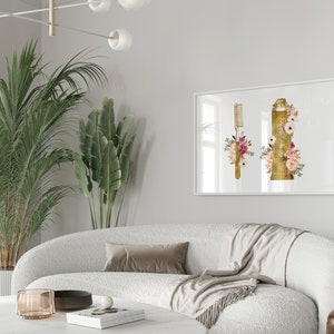 May include: A white framed print with a gold toothbrush and tube of toothpaste with floral accents. The print is hanging on a white wall above a white couch with a throw blanket and pillows.