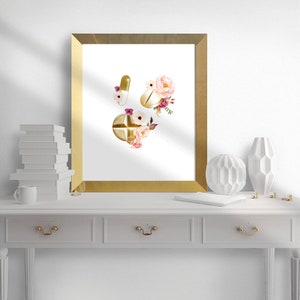 May include: A gold framed print with a watercolor illustration of gold pills and pink and white flowers.