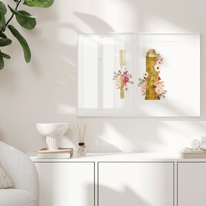 May include: A framed print with a gold toothbrush and tube of toothpaste with floral accents. The flowers are pink, white, and yellow.