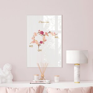 Pode incluir: Uma impress&atilde;o emoldurada branca com uma ilustra&ccedil;&atilde;o floral da estrutura qu&iacute;mica da dopamina. A impress&atilde;o est&aacute; pendurada em uma parede rosa claro acima de uma c&ocirc;moda branca com uma figura de anjo de cer&acirc;mica branca, uma l&acirc;mpada de m&aacute;rmore branco com um abajur branco e duas velas.