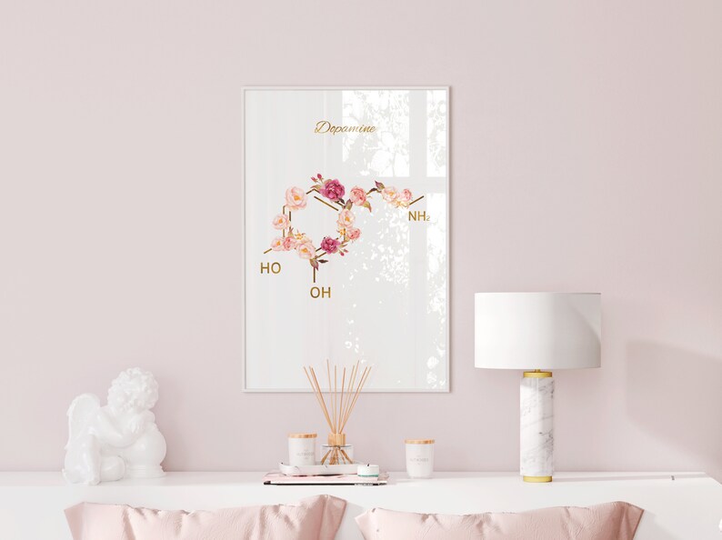 Pode incluir: Uma impress&atilde;o emoldurada branca com uma ilustra&ccedil;&atilde;o floral da estrutura qu&iacute;mica da dopamina. A impress&atilde;o est&aacute; pendurada em uma parede rosa claro acima de uma c&ocirc;moda branca com uma figura de anjo de cer&acirc;mica branca, uma l&acirc;mpada de m&aacute;rmore branco com um abajur branco e duas velas.