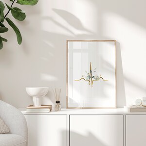 May include: A gold EKG line with a floral design in the center. The letters P, Q, R, S, and T are labeled on the EKG line. The print is framed in a light wood frame and is hanging on a white wall.