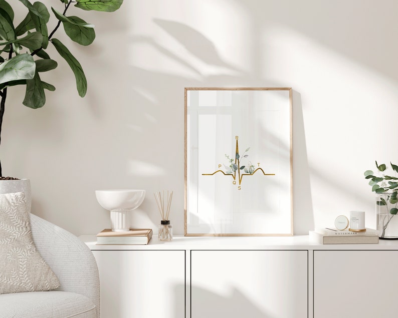 May include: A gold EKG line with a floral design in the center. The letters P, Q, R, S, and T are labeled on the EKG line. The print is framed in a light wood frame and is hanging on a white wall.