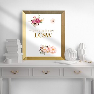 May include: A gold framed print with a white background featuring a floral design and the text "Licensed Clinical Social Worker LCSW".