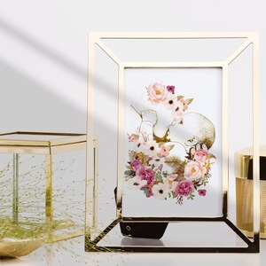 May include: A gold-toned picture frame with a white mat and a watercolor print of a baby surrounded by pink and white flowers.