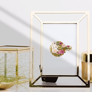May include: A gold-toned metal picture frame with a white mat and a floral print inside. The frame is sitting on a table with other gold-toned decorative items.