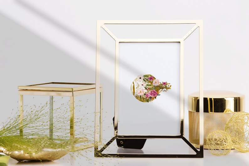 May include: A gold-toned metal picture frame with a white mat and a floral print inside. The frame is sitting on a table with other gold-toned decorative items.