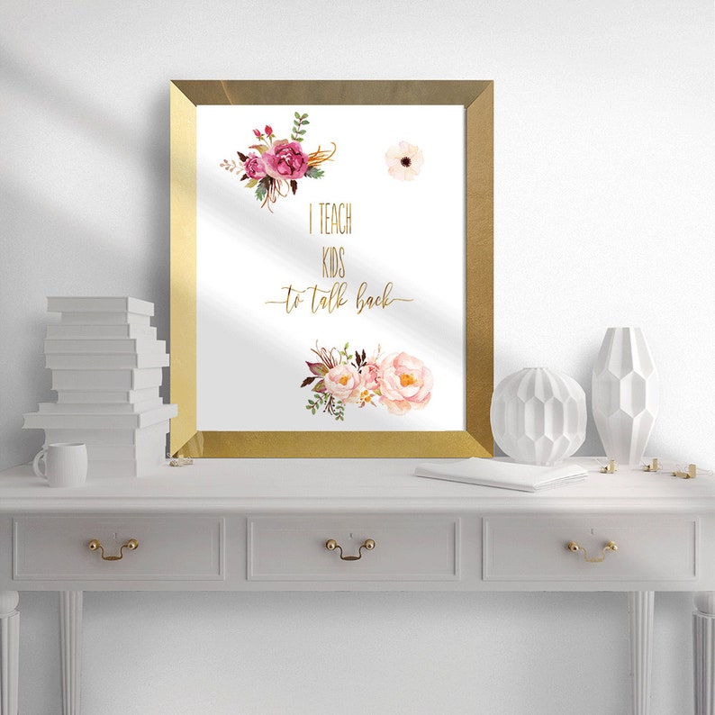May include: A gold framed print with a white background and pink and white flowers. The text on the print reads "I teach kids to talk back".