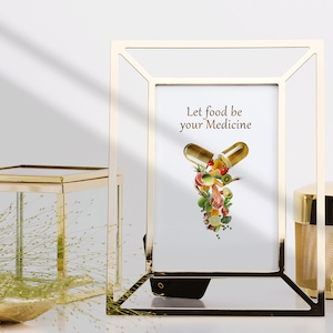 May include: Gold picture frame with a white background and the text "Let food be your medicine". Inside the frame is a graphic of a pill capsule with various fruits and vegetables spilling out.