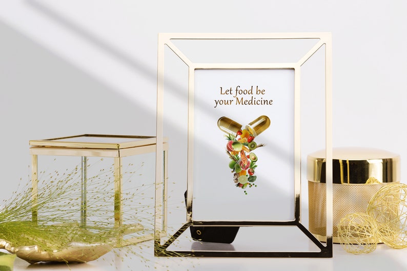 May include: Gold picture frame with a white background and the text "Let food be your medicine". Inside the frame is a graphic of a pill capsule with various fruits and vegetables spilling out.