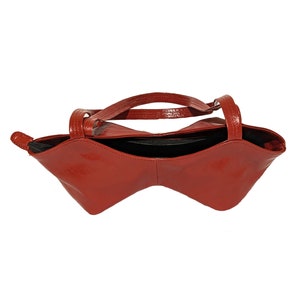 May include: A red leather handbag with a unique, curved shape and two top handles.