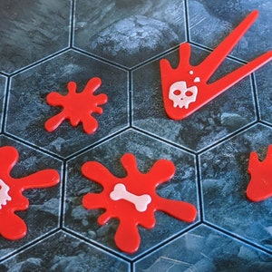 May include: Red game pieces with white skull and bone designs. The pieces are in the shape of splatters and arrows. The game pieces are on a hexagonal tile board with a blue and gray pattern.