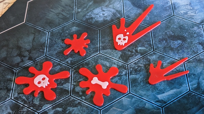 May include: Red game pieces with white skull and bone designs. The pieces are in the shape of splatters and arrows. The game pieces are on a hexagonal tile board with a blue and gray pattern.