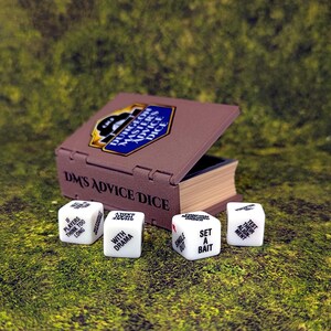 May include: A brown box with the text "DM'S ADVICE DICE" and a blue and gold emblem, open to reveal a stack of pages. Four white dice with phrases like "SET A BAIT" and "WITH DRAMA" are scattered around the box on a green surface.