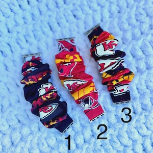 May include: Three watch bands with a repeating pattern of red, yellow, and white team logos. The bands are numbered 1, 2, and 3. The background is a light blue, textured surface.