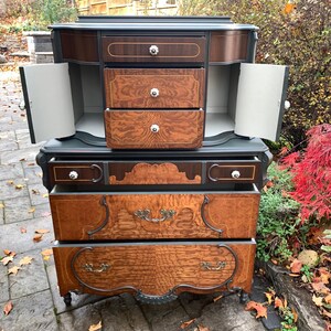 Puede incluir: Una c&oacute;moda vintage con un acabado de pintura verde oscuro y cajones de chapa de madera. La c&oacute;moda tiene una secci&oacute;n superior con dos puertas que se abren para revelar tres cajones. La secci&oacute;n inferior tiene cuatro cajones con herrajes ornamentados. La c&oacute;moda est&aacute; sentada en un patio de piedra.