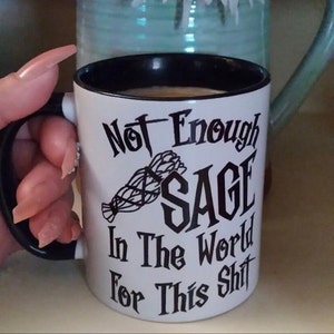 May include: White ceramic mug with a black rim and handle. The mug has black text that reads "Not Enough Sage In The World For This Shit". A black and white image of a bundle of sage is in the center of the mug.