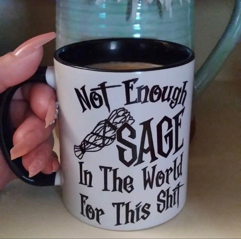 May include: White ceramic mug with a black rim and handle. The mug has black text that reads "Not Enough Sage In The World For This Shit". A black and white image of a bundle of sage is in the center of the mug.