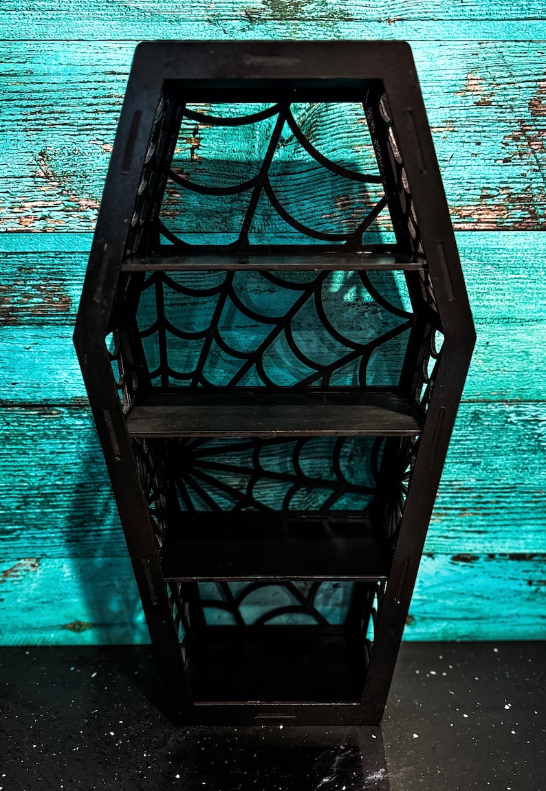May include: Black coffin-shaped shelf with a spiderweb design. The shelf has four shelves.