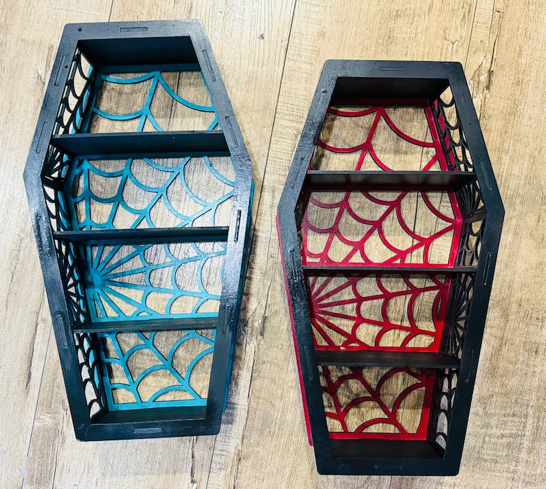 May include: Two black wooden coffin-shaped shelves with a spiderweb design. One shelf is painted teal blue and the other is painted red.
