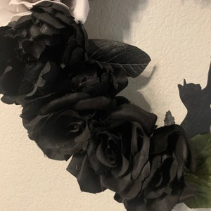 K&ouml;nnte beinhalten: Ein Kranz aus schwarzen Seidenrosen mit gr&uuml;nen Bl&auml;ttern. Die Rosen sind kreisf&ouml;rmig angeordnet und sehr voll.