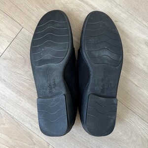 Puede incluir: Un par de mocasines de cuero negro, suelas hacia arriba, con el nombre de la marca "Salvatore Ferragamo" grabado en la suela. Las suelas tienen un dise&ntilde;o texturizado y muestran signos de desgaste.