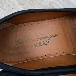 Puede incluir: Primer plano del interior de un zapato negro. La plantilla del zapato es de cuero marr&oacute;n con las palabras "Salvatore Ferragamo SPORT MADE IN ITALY" impresas en verde.
